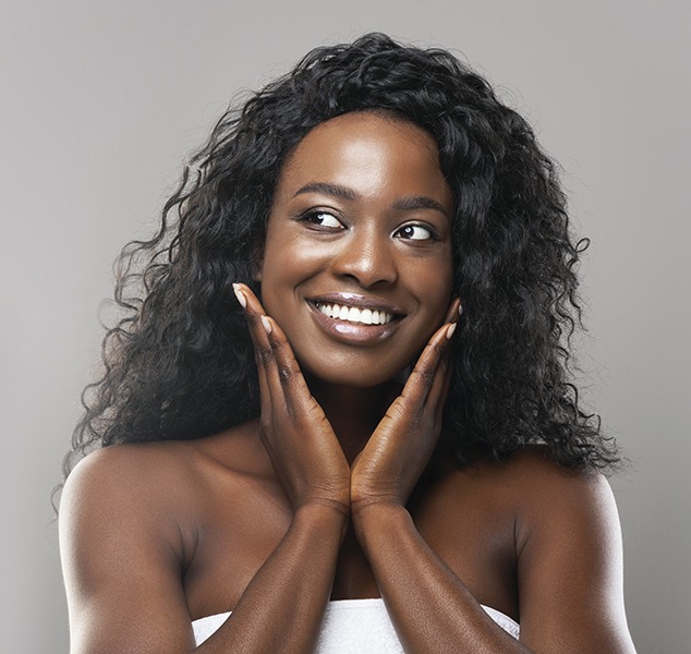 Dark skinned woman with nice skin feeling face, smiling